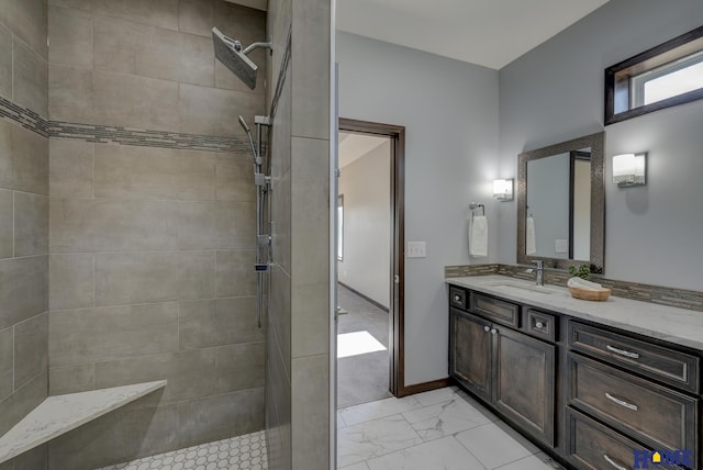 full bath with marble finish floor, baseboards, tiled shower, and vanity