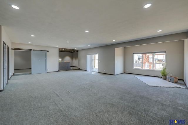 unfurnished living room with a wealth of natural light, carpet flooring, recessed lighting, and a barn door