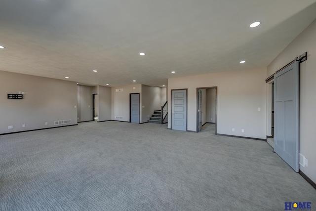 empty room with a barn door, visible vents, stairway, and recessed lighting