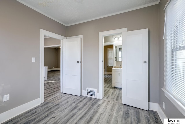 unfurnished bedroom with ensuite bathroom, sink, crown molding, a textured ceiling, and light wood-type flooring