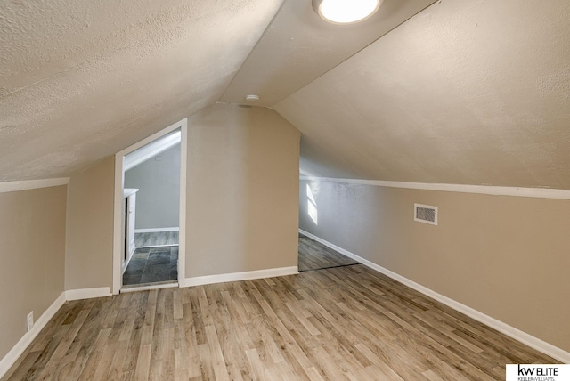 additional living space featuring hardwood / wood-style flooring, lofted ceiling, and a textured ceiling