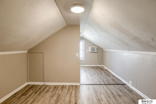 bonus room featuring a wall unit AC, lofted ceiling, hardwood / wood-style floors, and a textured ceiling