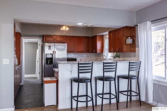 kitchen with a wealth of natural light, decorative backsplash, a kitchen breakfast bar, and stainless steel fridge with ice dispenser