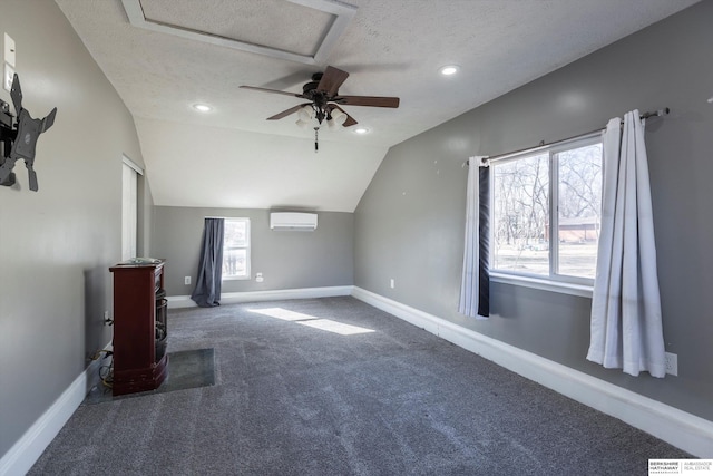 additional living space with vaulted ceiling, a wall mounted air conditioner, dark colored carpet, ceiling fan, and a textured ceiling