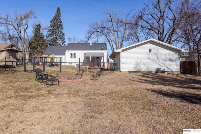 rear view of house featuring a playground, a lawn, and an outdoor fire pit