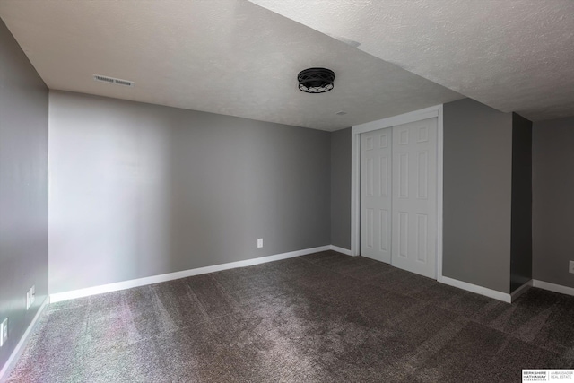 additional living space featuring dark carpet and a textured ceiling