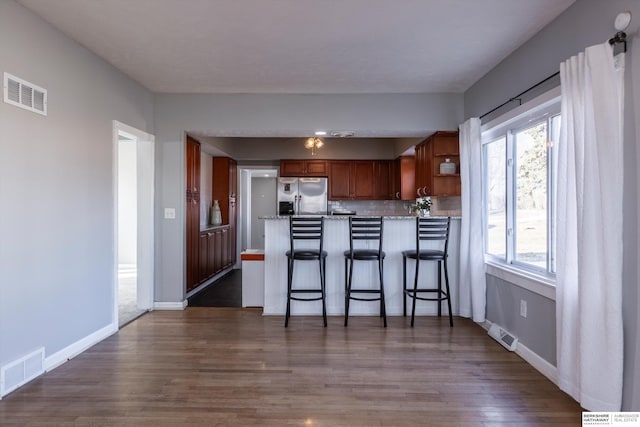 kitchen with dark wood-type flooring, tasteful backsplash, a kitchen bar, stainless steel fridge with ice dispenser, and kitchen peninsula