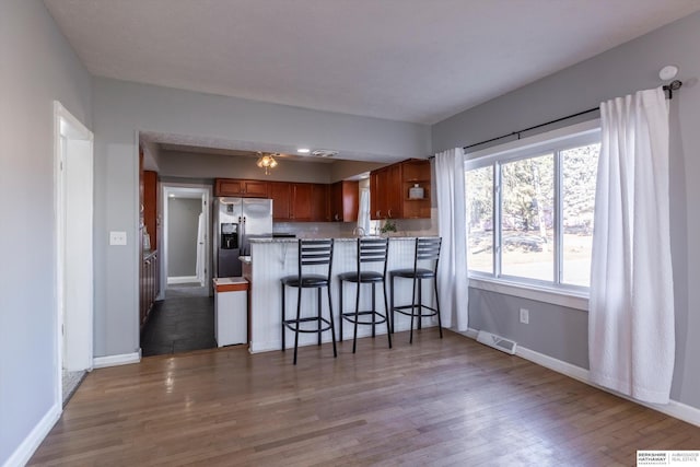 kitchen featuring wood-type flooring, stainless steel fridge, a kitchen bar, and kitchen peninsula