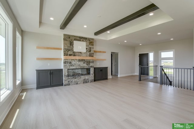 unfurnished living room with a stone fireplace, light wood-type flooring, and beam ceiling