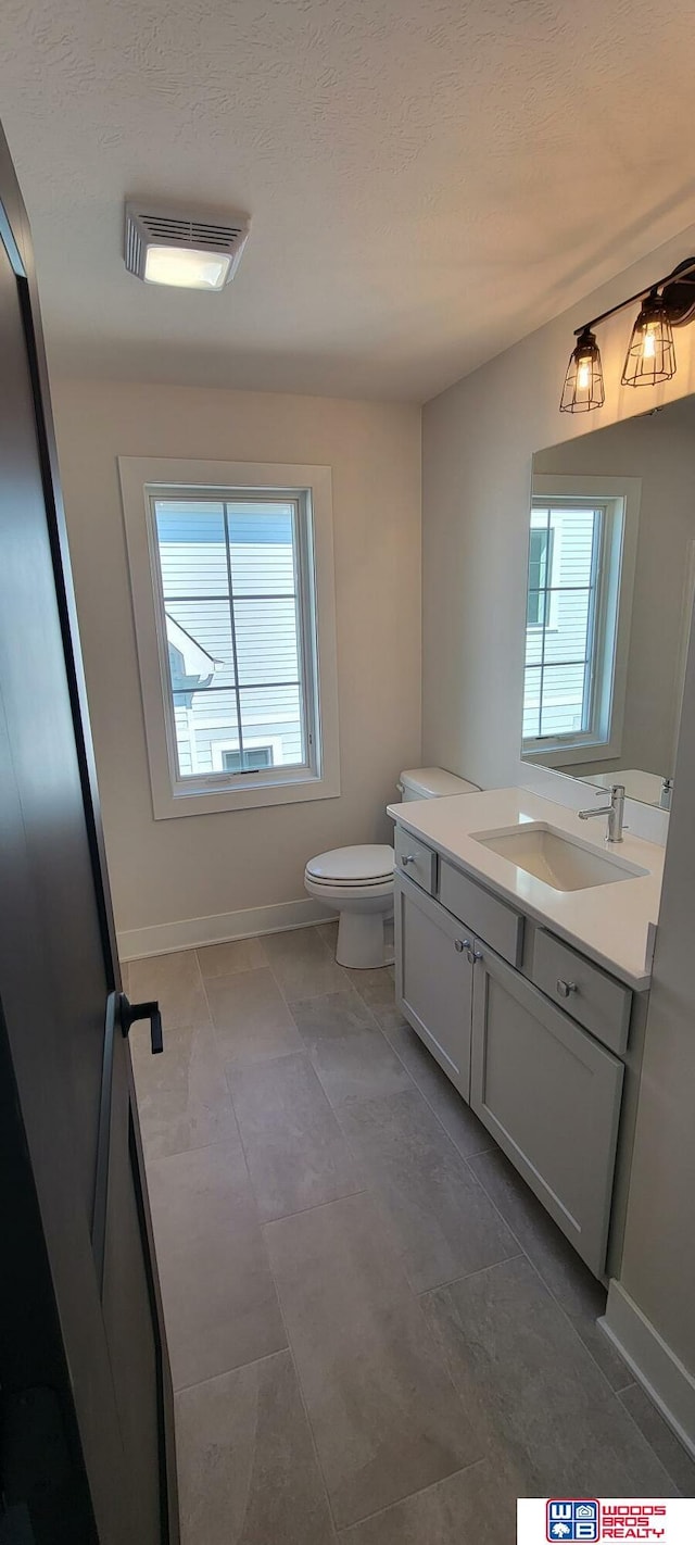 bathroom featuring vanity, a wealth of natural light, a textured ceiling, and toilet