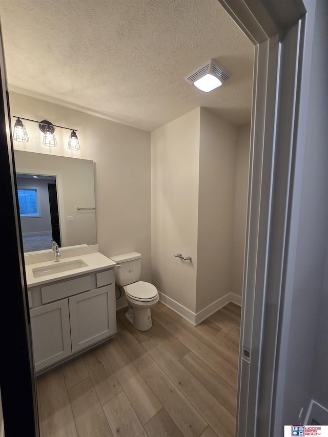 bathroom with wood-type flooring, toilet, vanity, and a textured ceiling