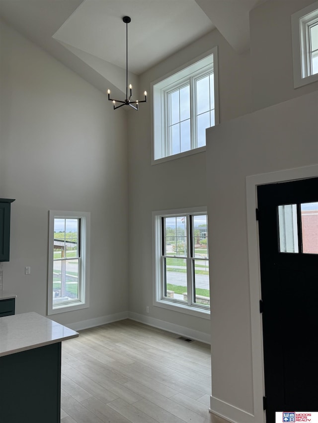 foyer entrance featuring a notable chandelier, a healthy amount of sunlight, a towering ceiling, and light wood-type flooring