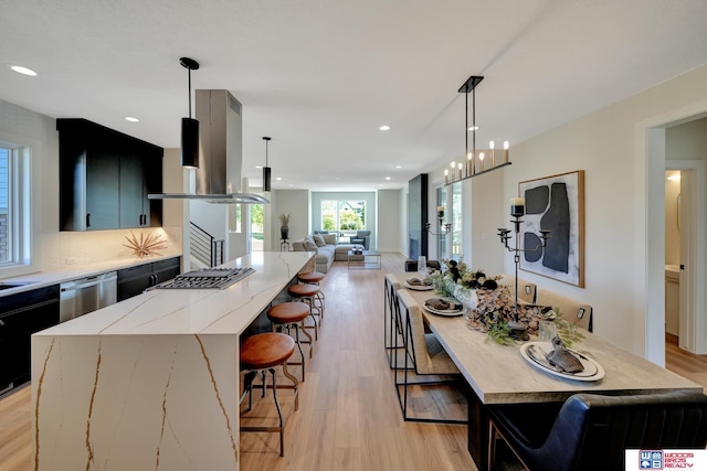 kitchen with appliances with stainless steel finishes, pendant lighting, island range hood, and light hardwood / wood-style flooring