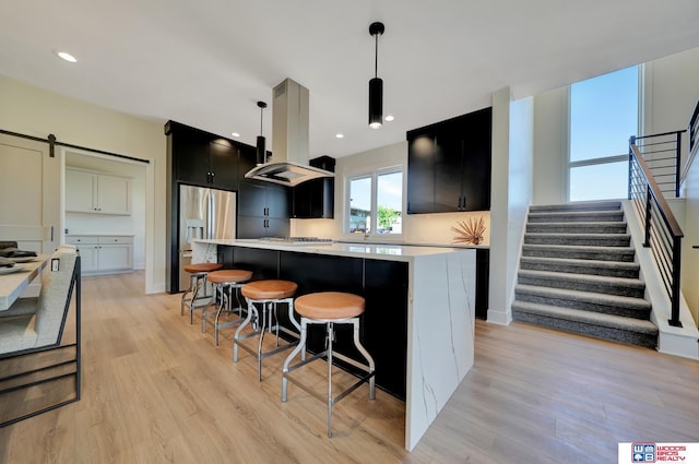 kitchen featuring a kitchen island, island range hood, hanging light fixtures, stainless steel appliances, and a barn door