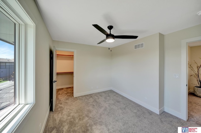 unfurnished bedroom featuring a walk in closet, light carpet, ceiling fan, and a closet