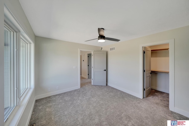 unfurnished bedroom with a spacious closet, light colored carpet, a closet, and ceiling fan