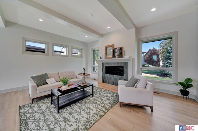 living area with light wood finished floors, a tiled fireplace, beam ceiling, and baseboards