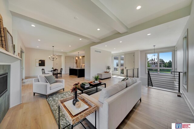 living area with recessed lighting, light wood-style flooring, a tiled fireplace, an inviting chandelier, and beamed ceiling