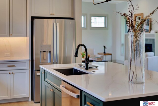 kitchen featuring stainless steel appliances, a kitchen island with sink, a sink, and light stone counters