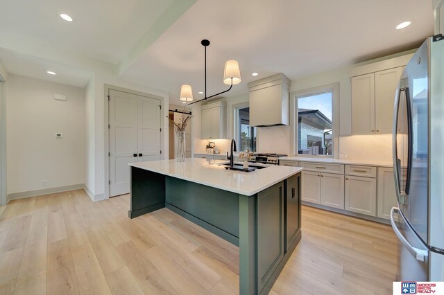 kitchen featuring a kitchen island with sink, a sink, light countertops, light wood-type flooring, and freestanding refrigerator