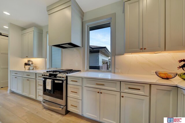 kitchen featuring stainless steel range with gas cooktop, tasteful backsplash, light countertops, a barn door, and premium range hood