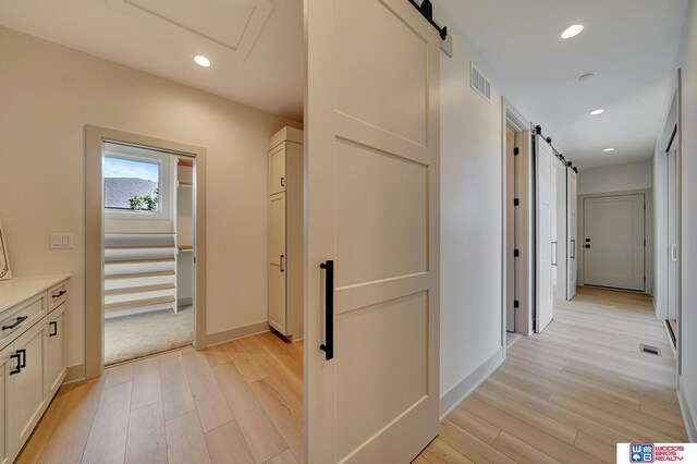 corridor featuring recessed lighting, visible vents, light wood-style flooring, and a barn door