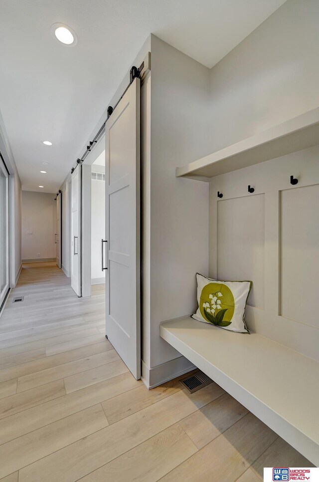 mudroom with a barn door, visible vents, light wood-style flooring, and recessed lighting