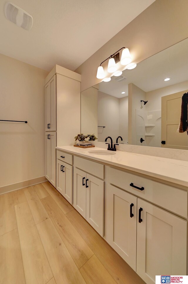 bathroom featuring visible vents, vanity, wood finished floors, baseboards, and walk in shower