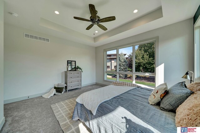 carpeted bedroom featuring ceiling fan, recessed lighting, visible vents, baseboards, and a tray ceiling