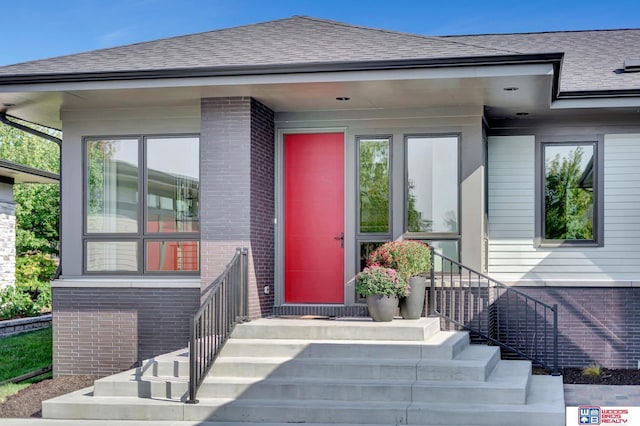 view of exterior entry featuring a shingled roof and brick siding