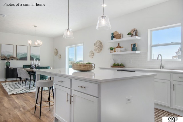 kitchen with pendant lighting, sink, a center island, white cabinets, and light wood-type flooring