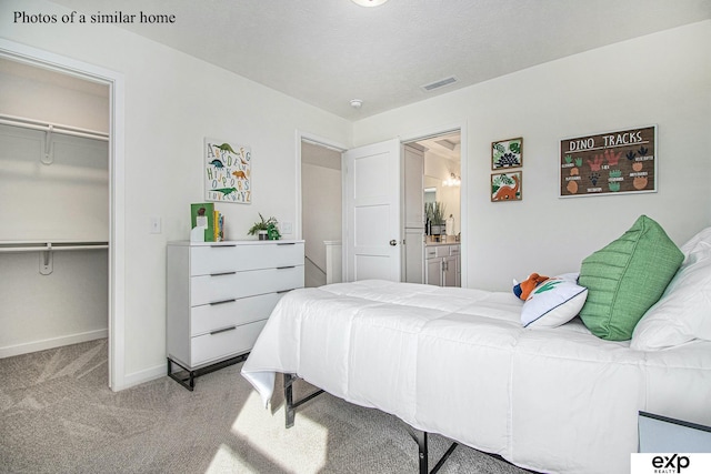 carpeted bedroom with a spacious closet, a closet, a textured ceiling, and ensuite bathroom