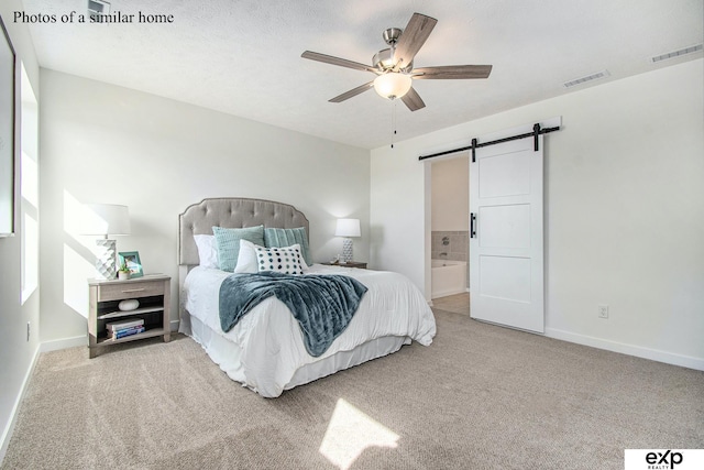 carpeted bedroom featuring ensuite bath, a textured ceiling, a barn door, and ceiling fan