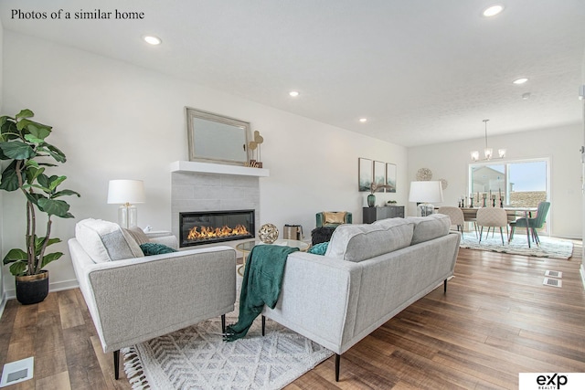 living room featuring an inviting chandelier, wood-type flooring, and a tiled fireplace