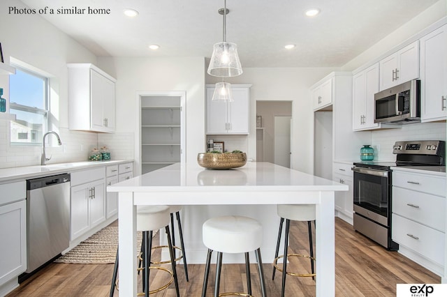 kitchen with white cabinetry, stainless steel appliances, sink, and pendant lighting