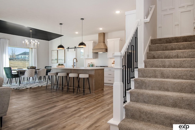 kitchen with a kitchen bar, hanging light fixtures, custom range hood, a kitchen island with sink, and white cabinets