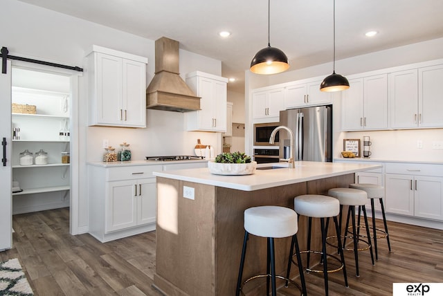 kitchen featuring custom exhaust hood, white cabinetry, stainless steel fridge with ice dispenser, an island with sink, and a barn door