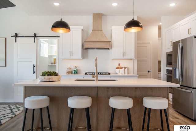 kitchen with stainless steel appliances, a kitchen island with sink, custom exhaust hood, and white cabinets