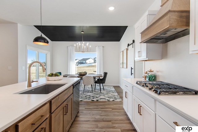 kitchen with sink, appliances with stainless steel finishes, white cabinetry, hanging light fixtures, and custom range hood