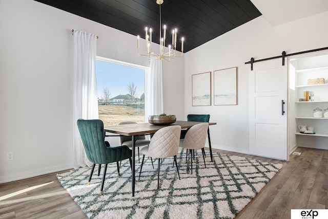 dining area featuring a notable chandelier, wood-type flooring, a barn door, and vaulted ceiling