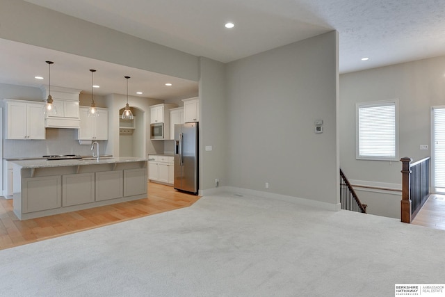 kitchen with sink, appliances with stainless steel finishes, white cabinetry, an island with sink, and decorative light fixtures