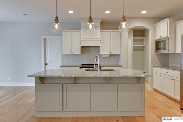 kitchen with white cabinetry, decorative light fixtures, stainless steel microwave, and an island with sink