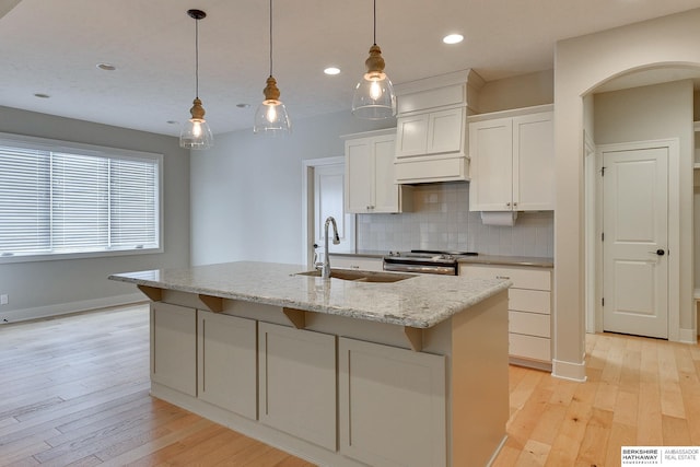 kitchen with white cabinetry, sink, decorative light fixtures, and a center island with sink