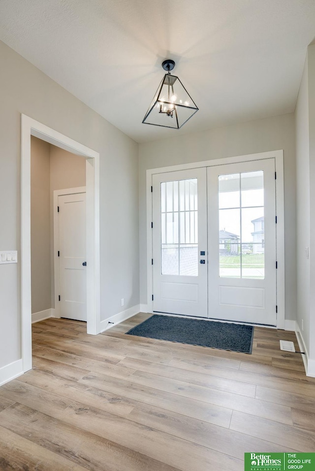 entryway featuring french doors, a chandelier, and light wood-type flooring