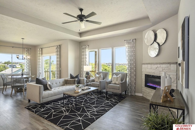 living room featuring a raised ceiling, wood-type flooring, a stone fireplace, and a textured ceiling