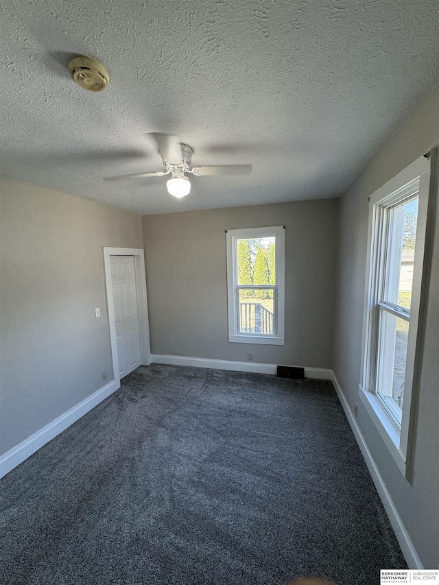 spare room featuring ceiling fan, dark carpet, and a textured ceiling