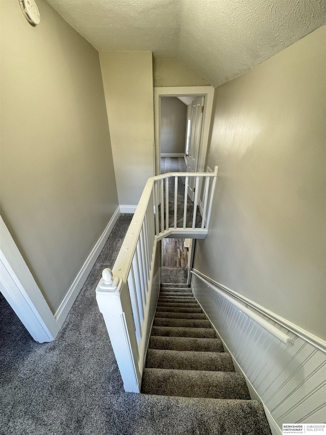 staircase with carpet flooring, vaulted ceiling, and a textured ceiling