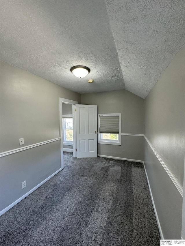 carpeted spare room featuring vaulted ceiling and a textured ceiling