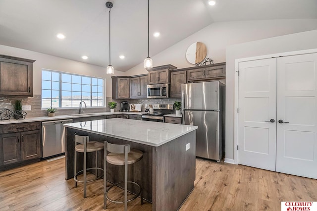 kitchen featuring sink, stainless steel appliances, dark brown cabinetry, a kitchen island, and decorative light fixtures