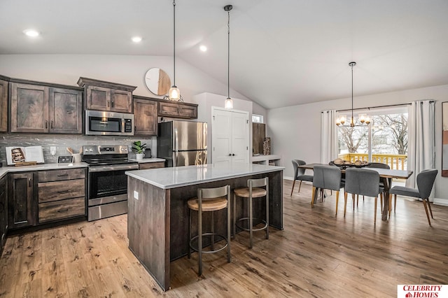 kitchen with a breakfast bar, appliances with stainless steel finishes, a center island, dark brown cabinetry, and decorative light fixtures